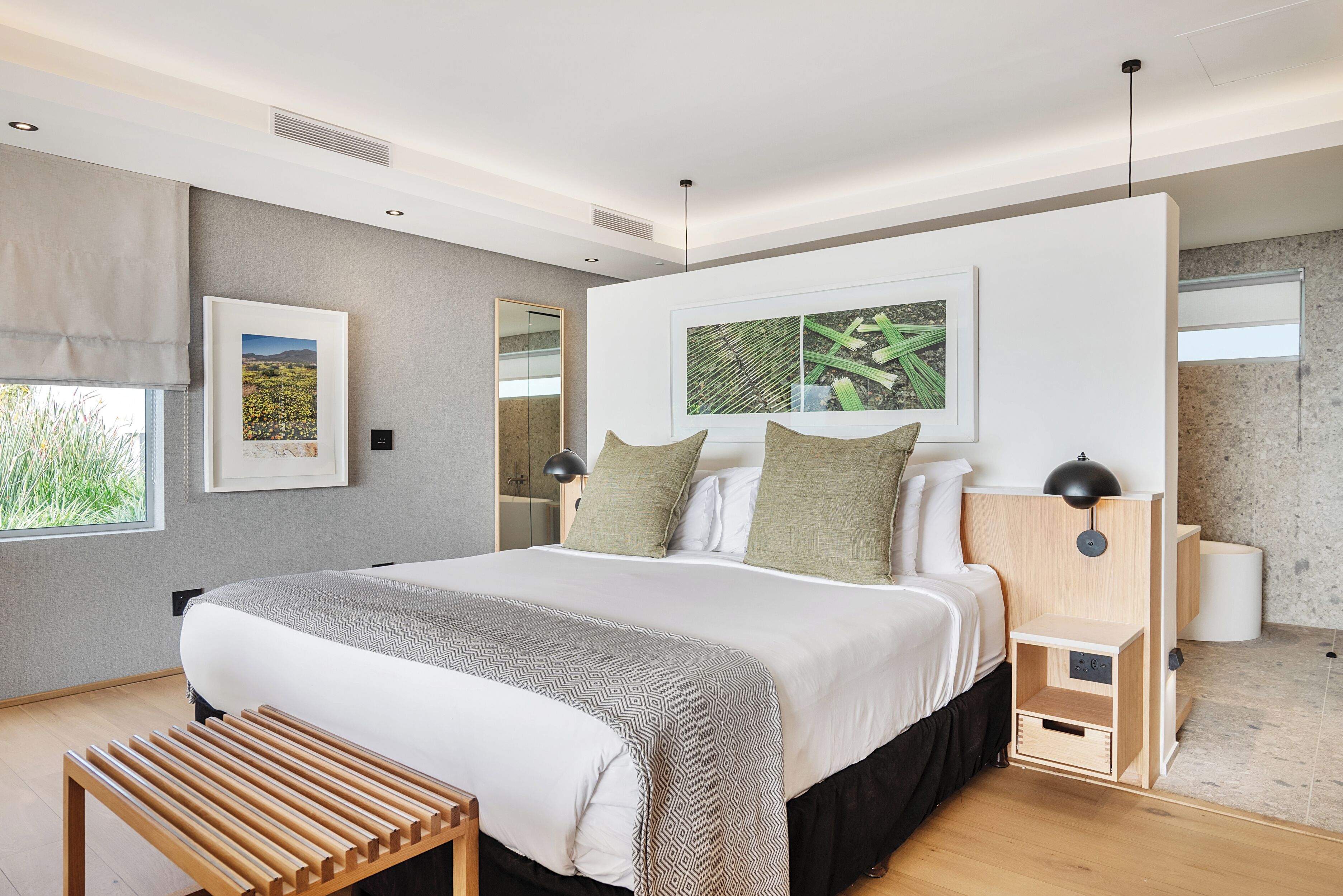 A modern bedroom with a large bed, a bedside table, a bench, and artwork on the wall.