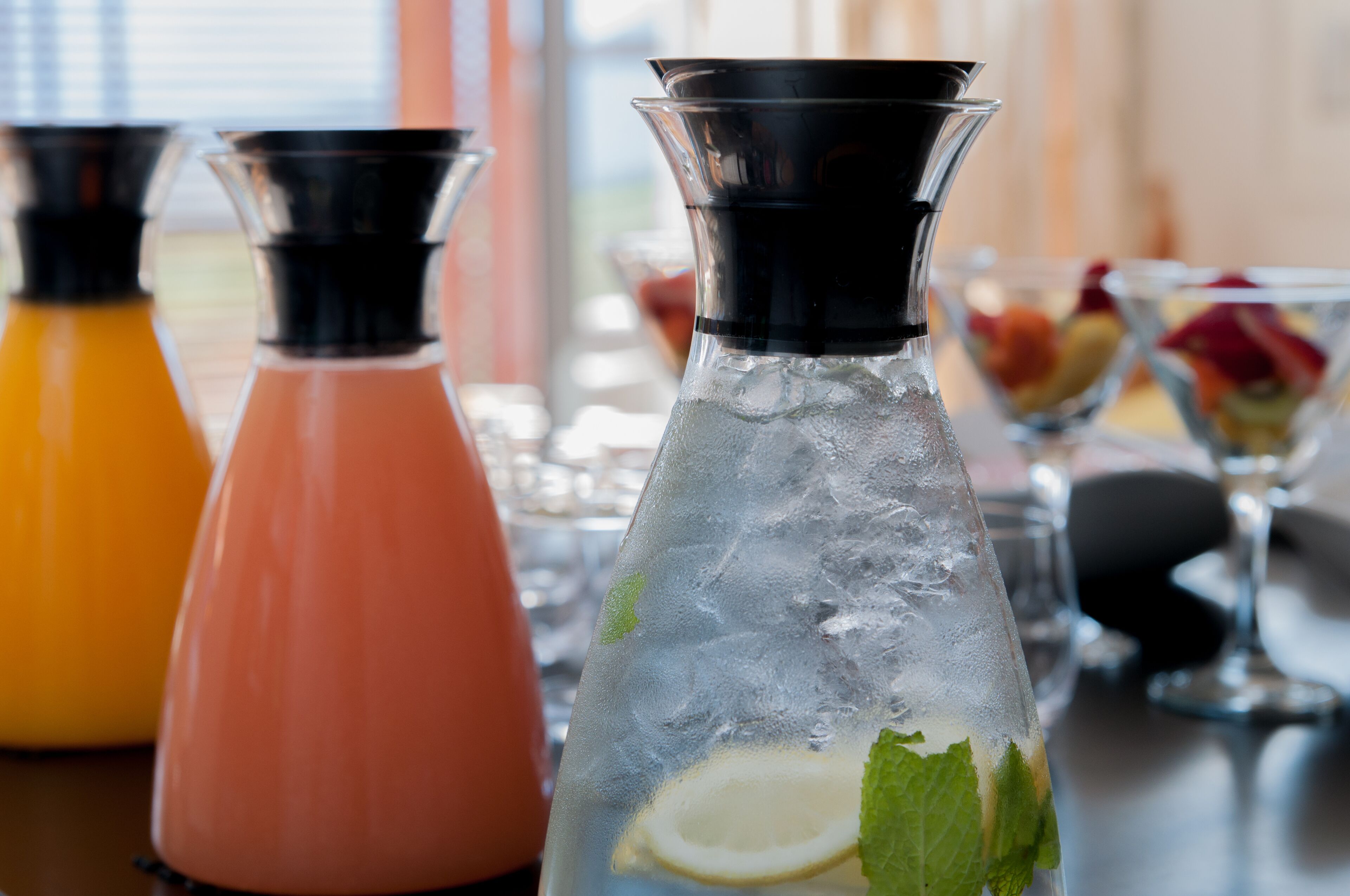 Three glass bottles with ice and garnishes, likely containing beverages, on a table with a blurred background.