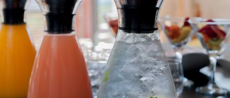 Three glass bottles with ice and garnishes, likely containing beverages, on a table with a blurred background.