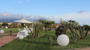 A garden with white tables and chairs, a white umbrella, and large white spherical decorations. - San Domenico Family Hotel (Scalea)