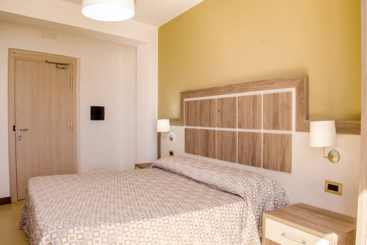 Ein Hotelzimmer mit Bett, Nachttischen, einem Holzkopfteil und Wandleuchten.