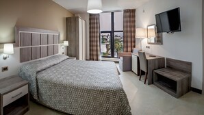 A hotel room with a bed, desk, TV, and a view of the city. - San Domenico Family Hotel (Scalea)