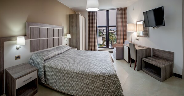 A hotel room with a bed, desk, TV, and a view of the city.