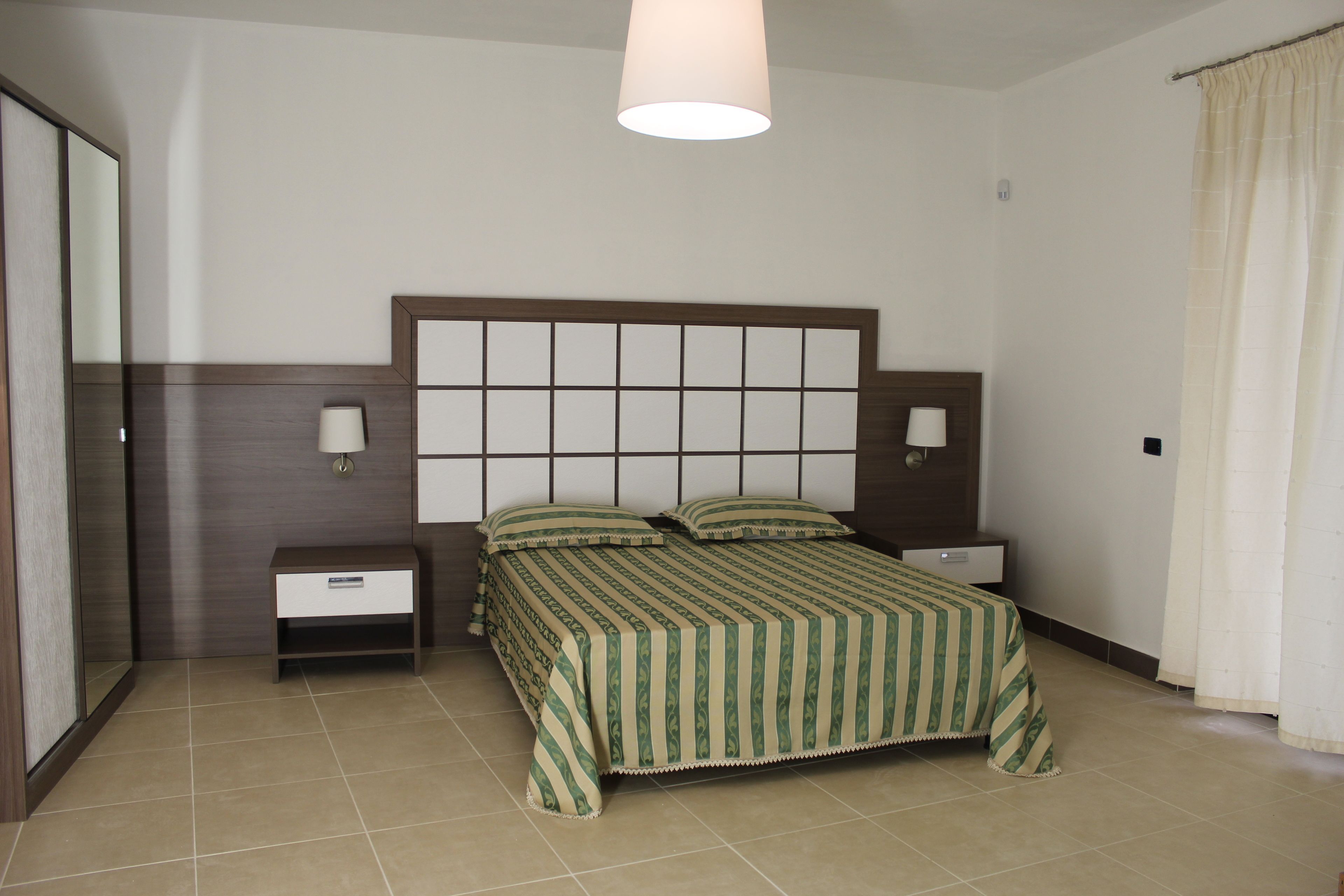 Een keurig opgemaakt slaapkamer met een bed, nachtkastjes en een hanglamp.