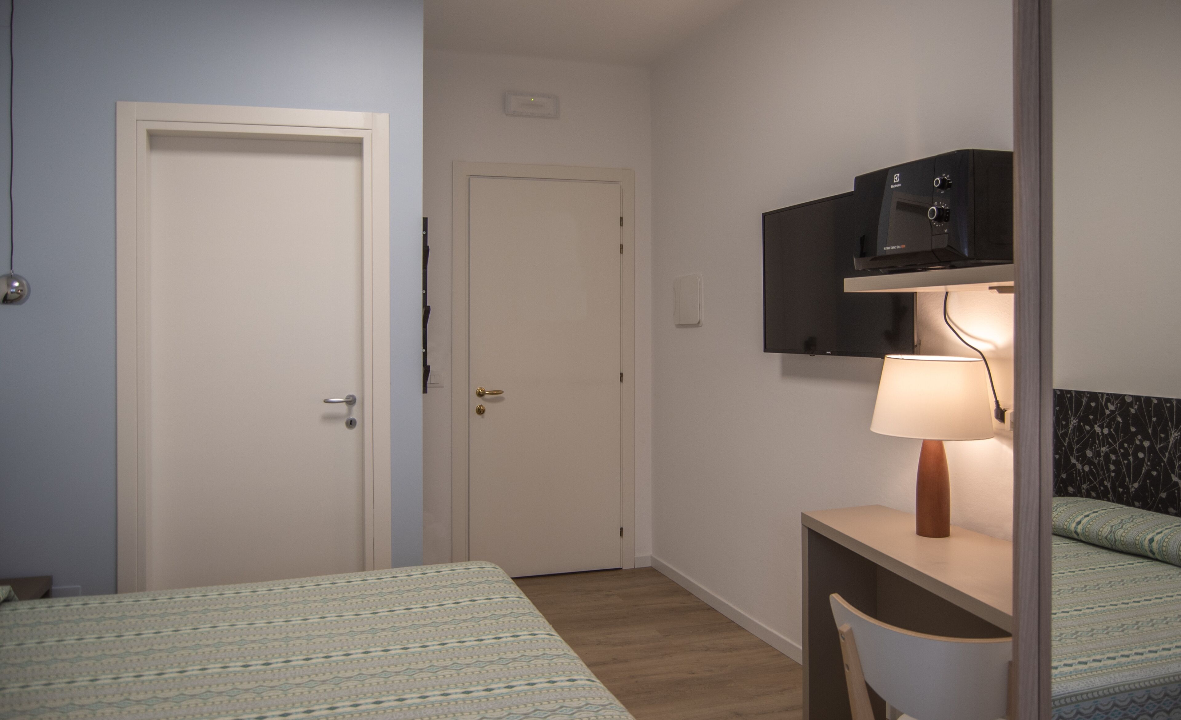 A hotel room with two beds, a desk with a lamp, a TV, and a wall-mounted shelf.