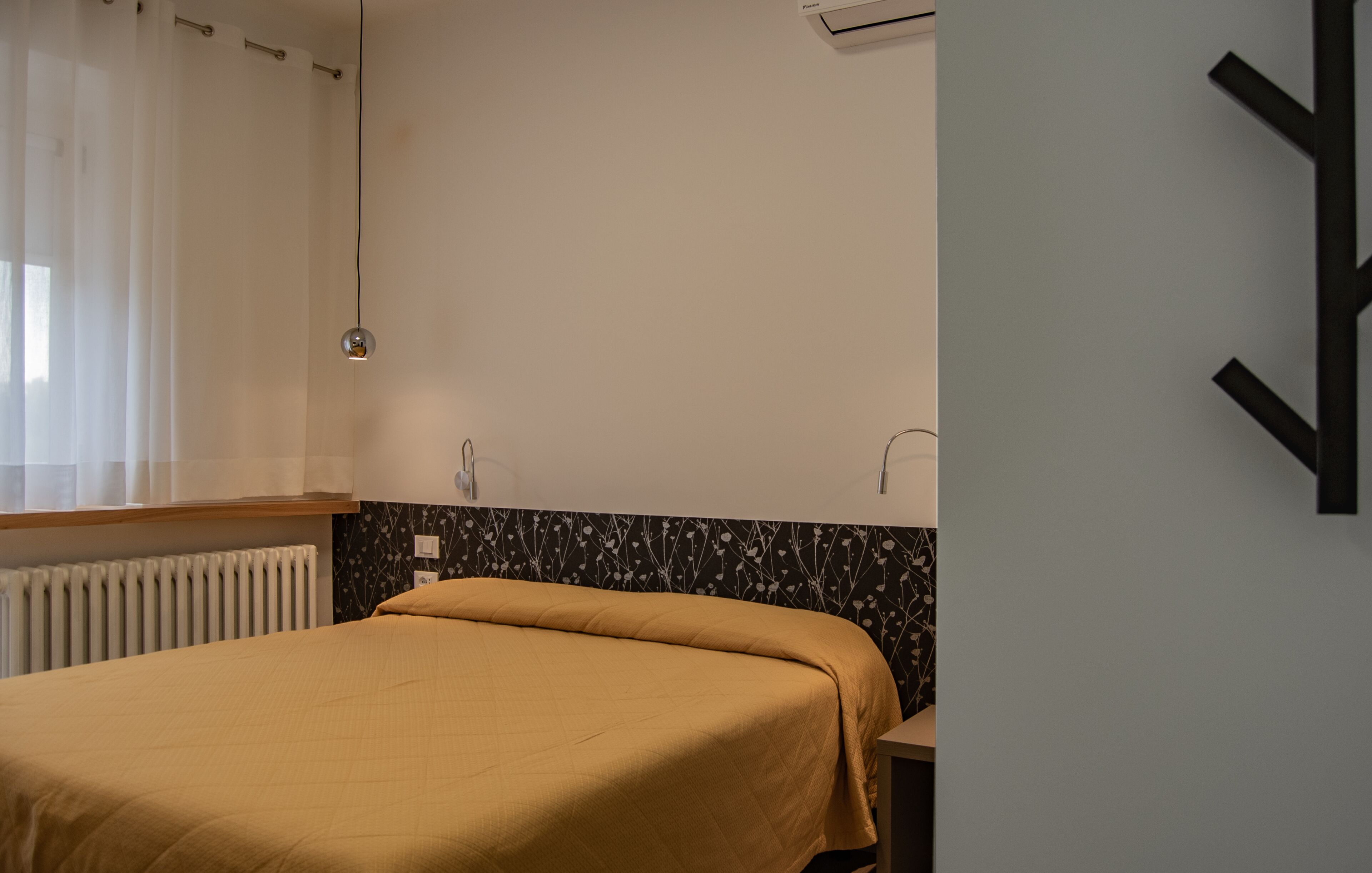 A bedroom with a bed, a radiator, a wall-mounted light, and a black and white patterned wall.