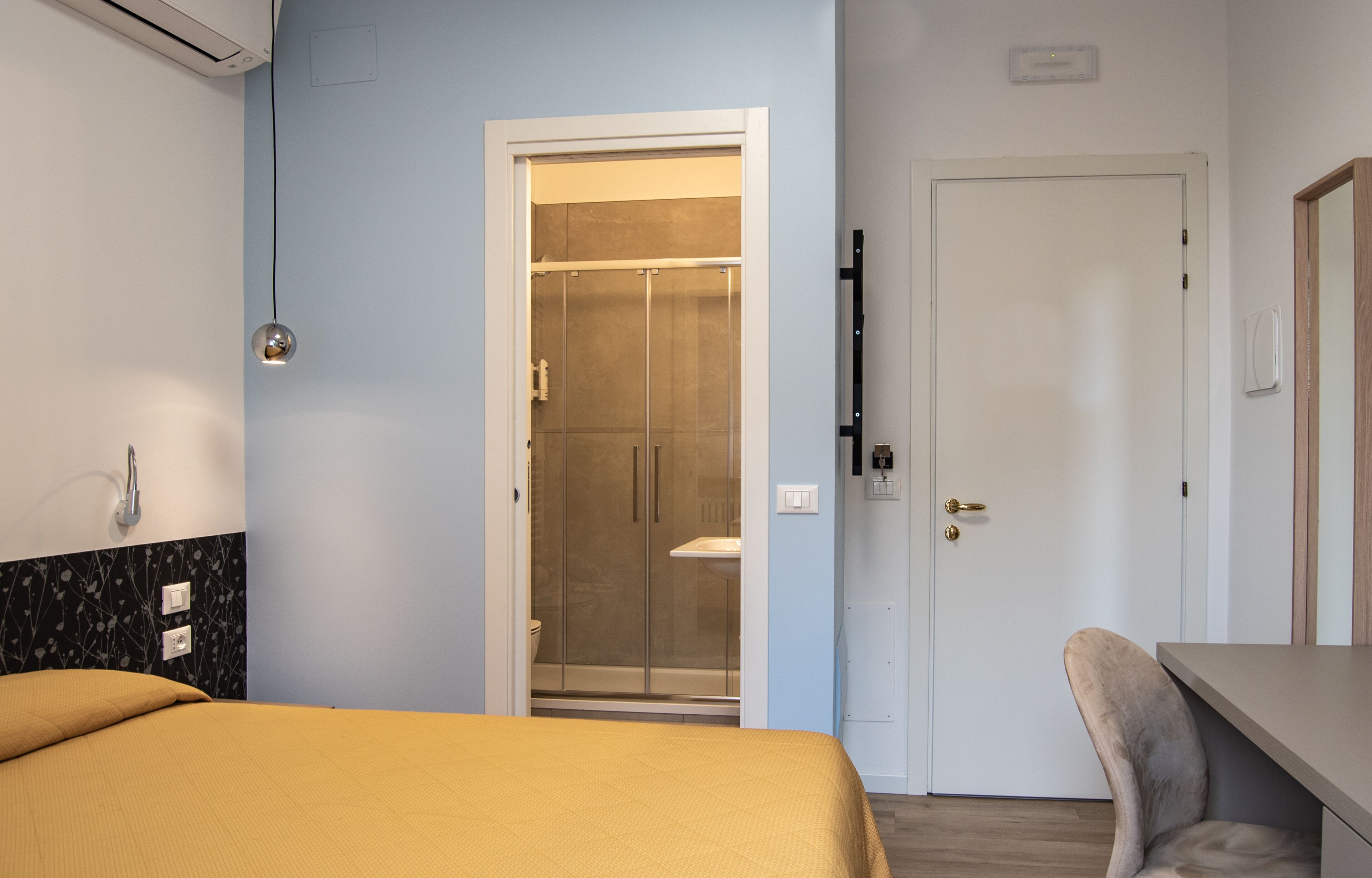 Une chambre d’hôtel avec un lit, un bureau, une chaise, une douche et une porte.