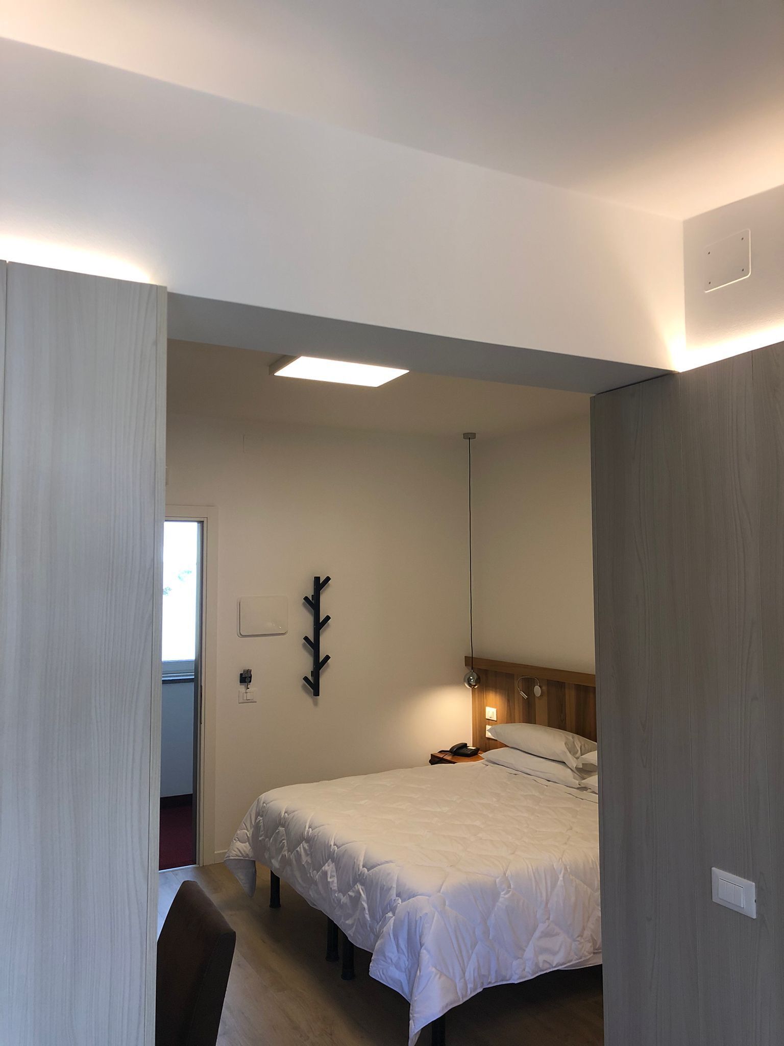 Quarto de hotel com cama, mesa de cabeceira, abajur e luminária na parede.