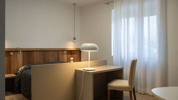 Ein Hotelzimmer mit Bett, Schreibtisch mit Lampe, Stuhl und einem fenster mit Vorhängen.