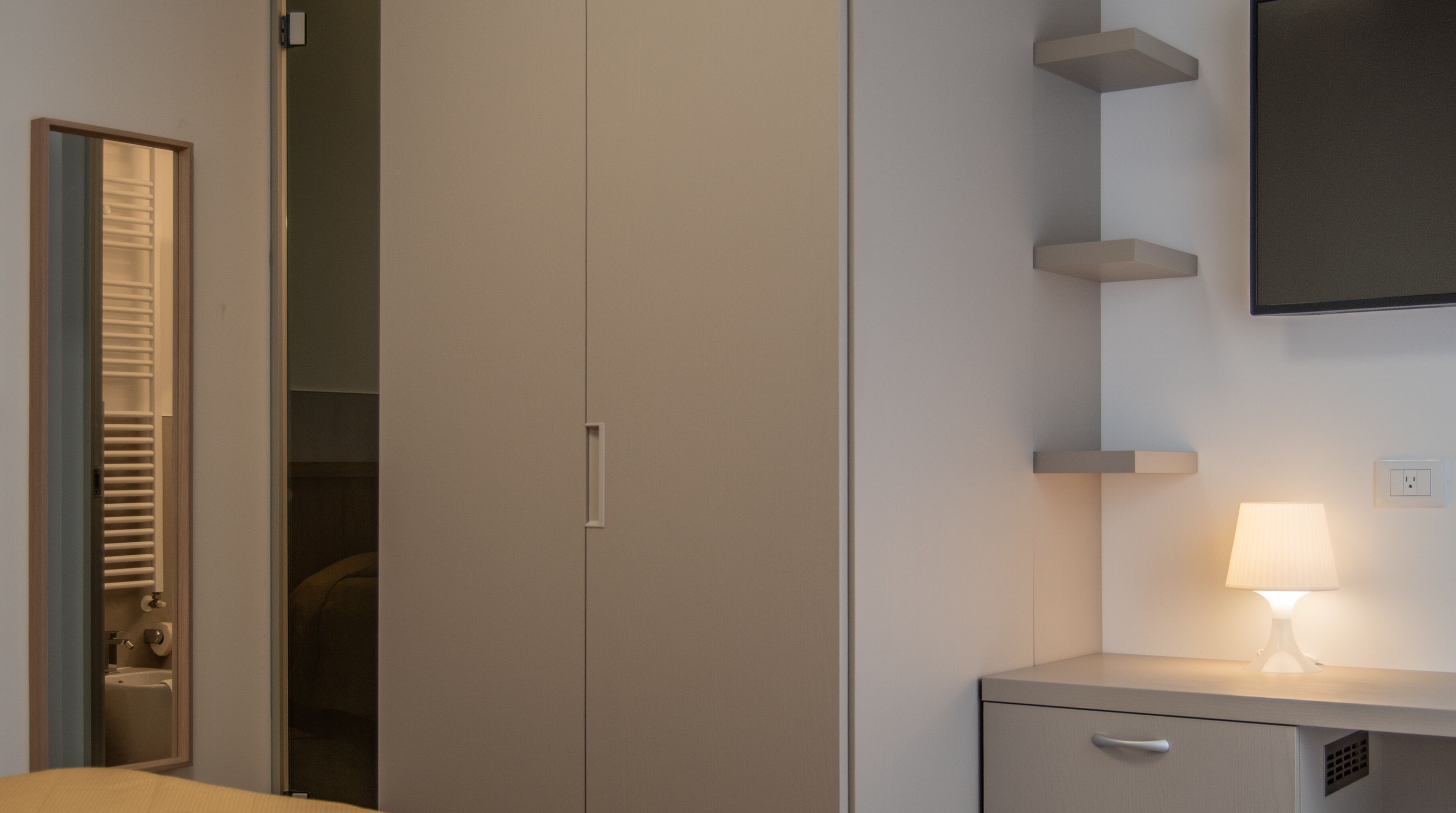 Une chambre avec une armoire, une table de chevet avec une lampe et un téléviseur fixé au mur.