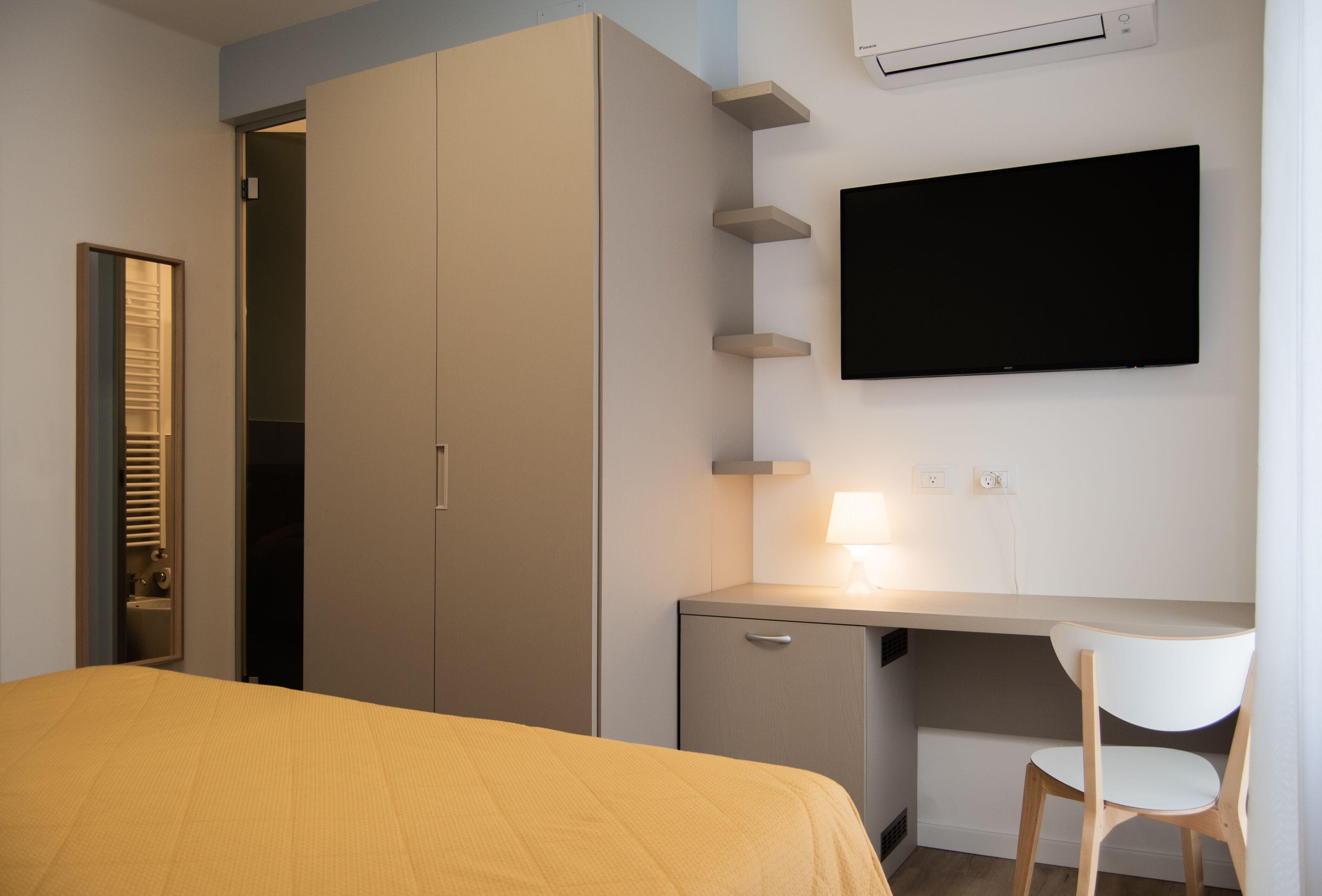 Ein Hotelzimmer mit einem Bett, einem Schreibtisch, einem Stuhl, einem Kleiderschrank und einem an der Wand befestigten Fernseher.