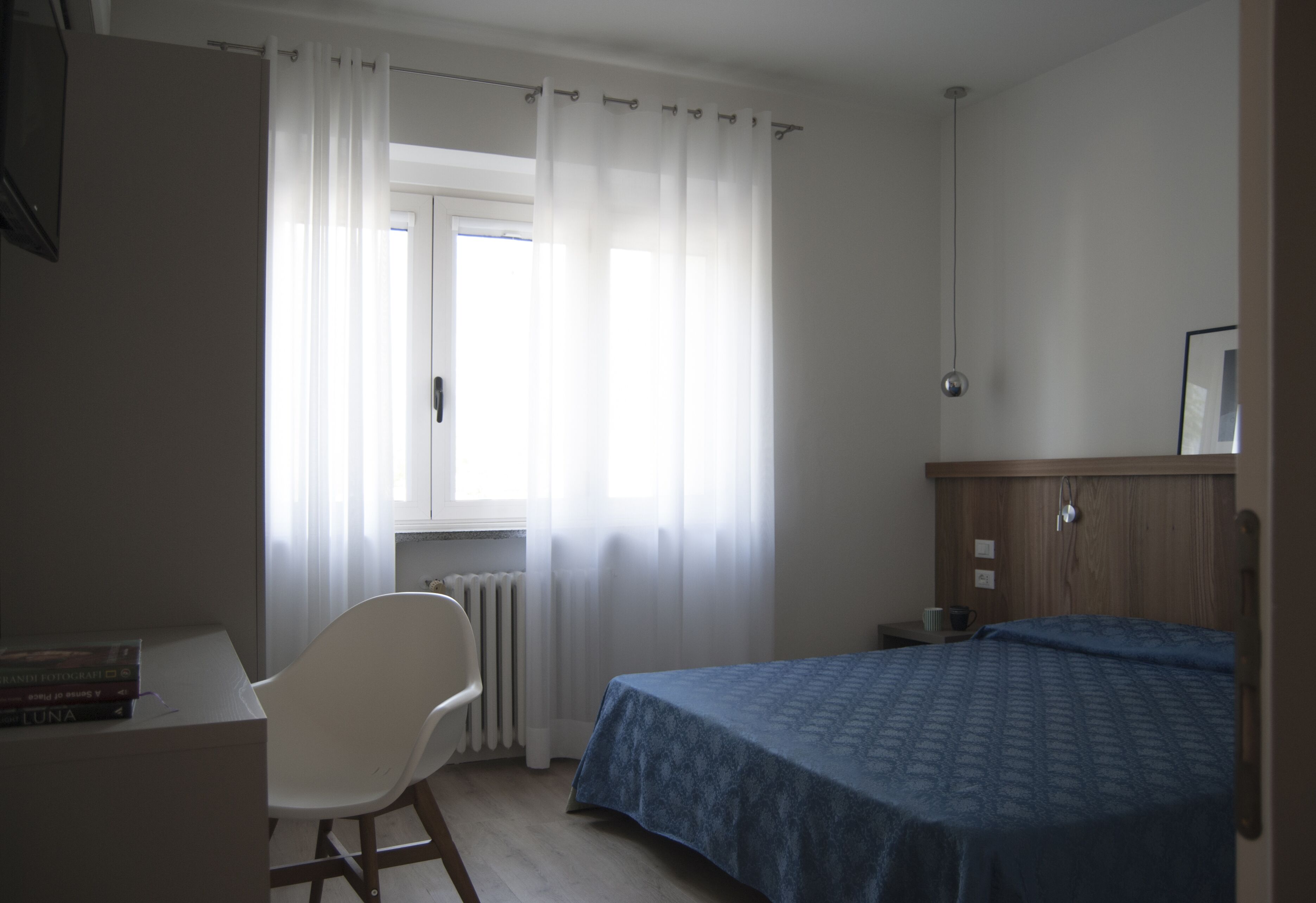 A bedroom with a bed, a chair, a radiator, and a window with curtains.