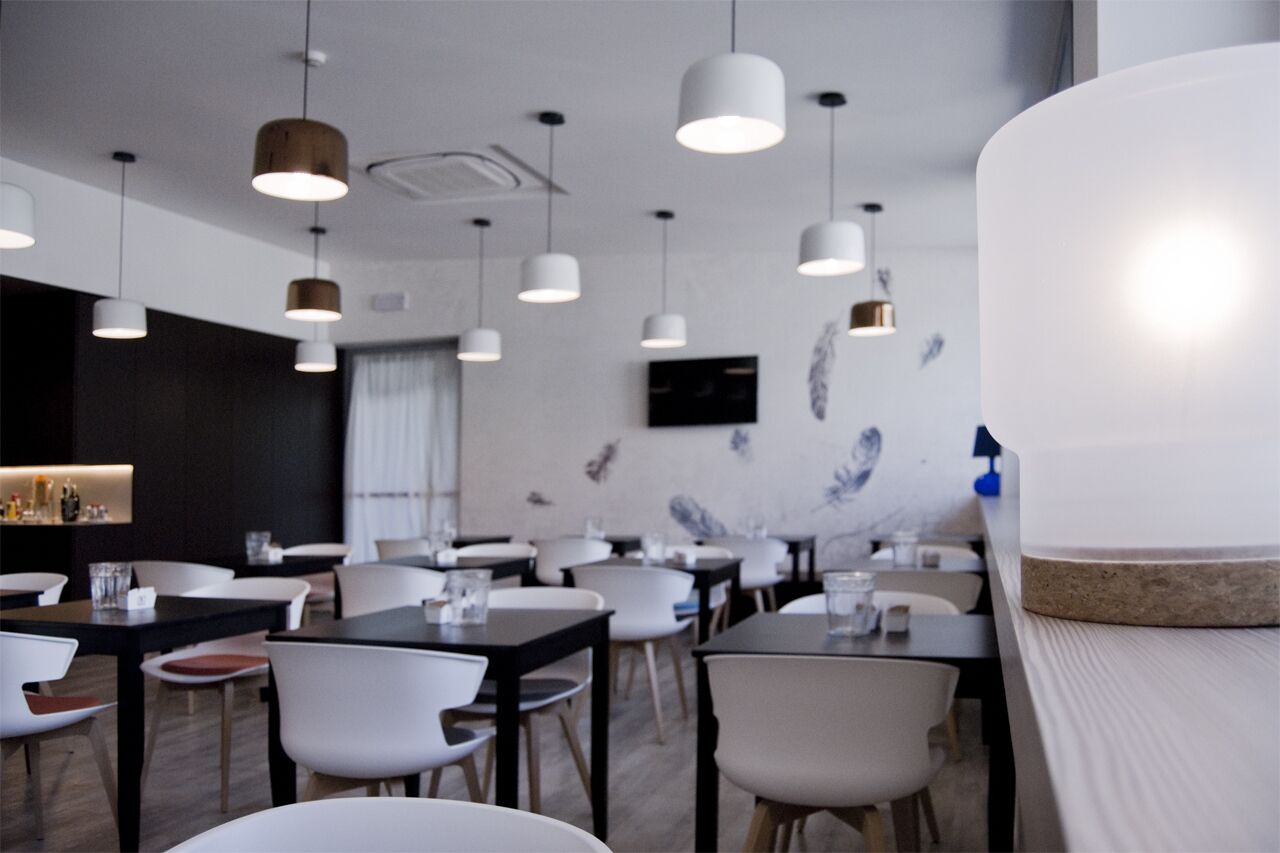 Een moderne eetruimte met witte stoelen en tafels, hanglampen en een aan de muur bevestigde televisie.