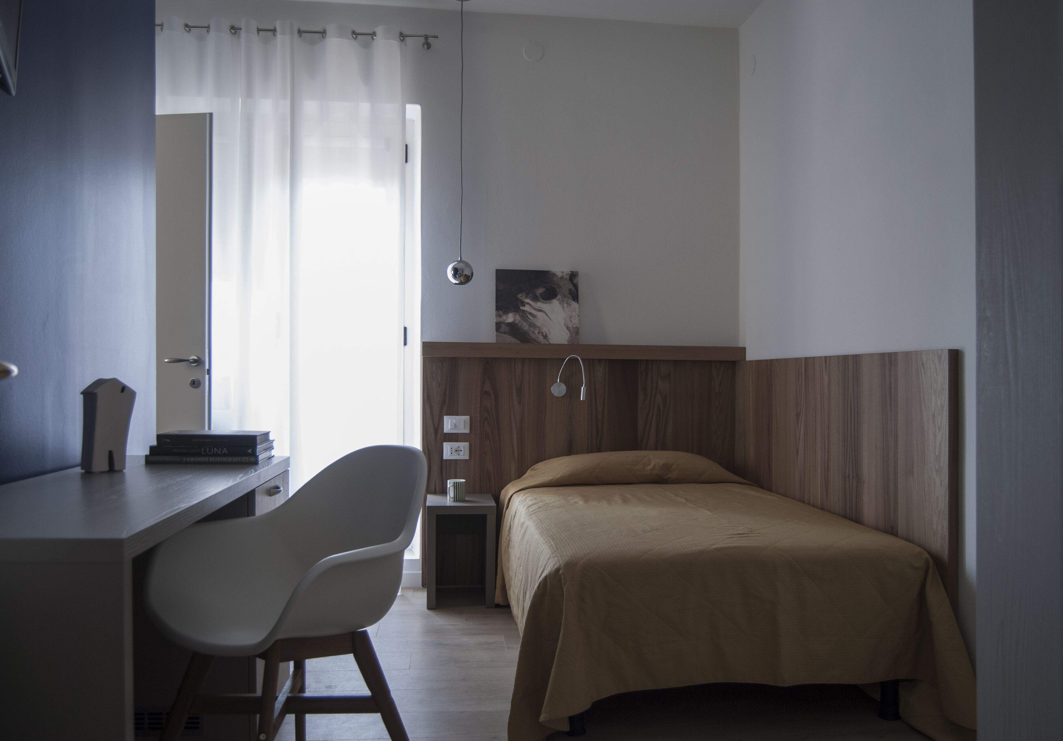 Une chambre à coucher comprenant un lit, un bureau, une chaise, une table de chevet et une lampe fixée au mur.