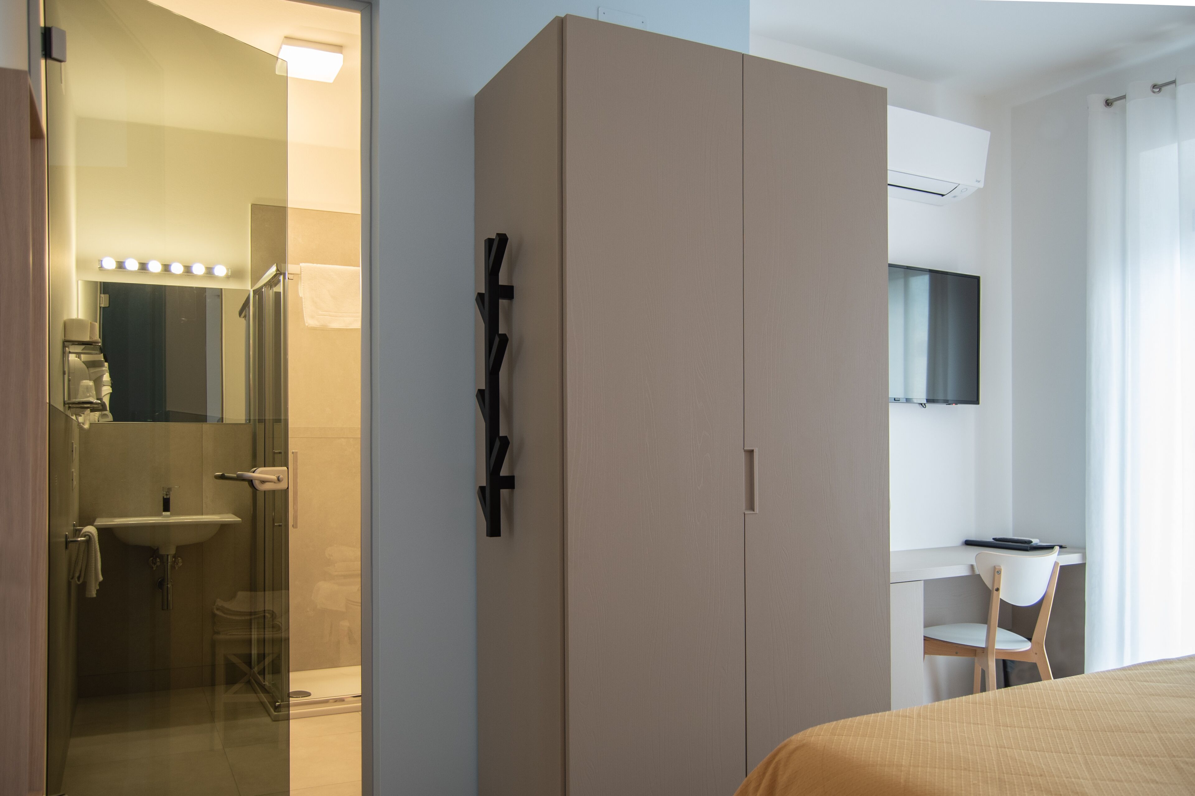 Une chambre d’hôtel moderne dotée d’une douche en verre, d’un lavabo, d’une armoire, d’un bureau avec une chaise et d’un lit.