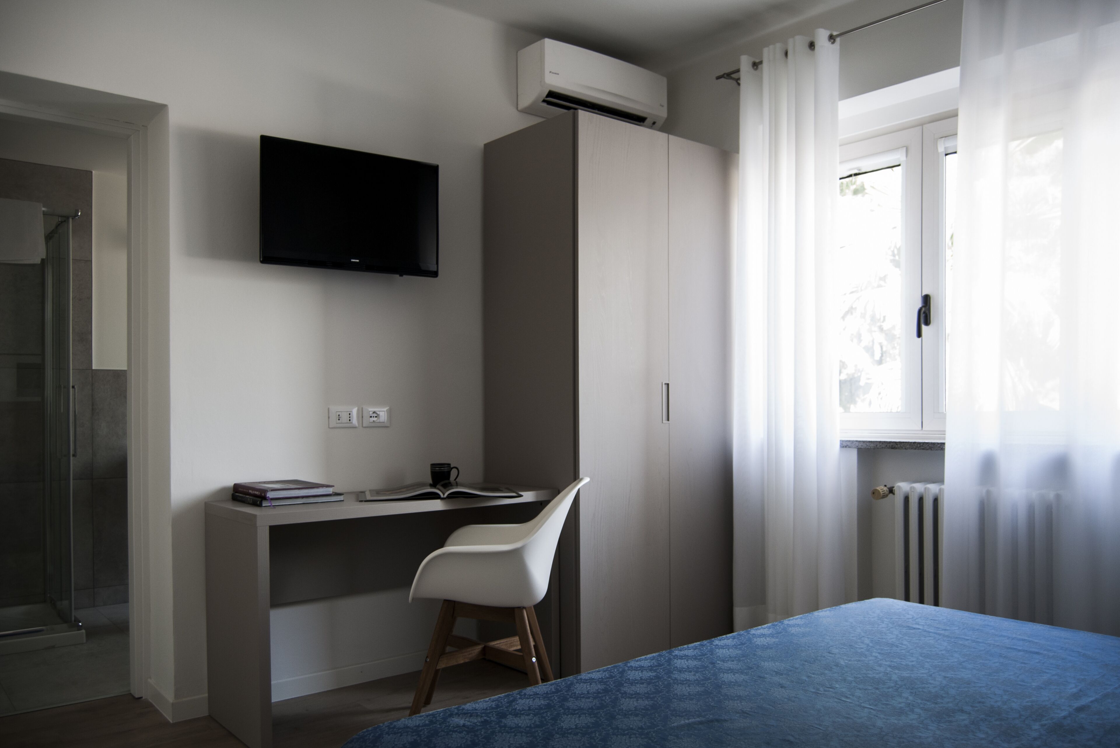 A bedroom with a bed, a desk, a chair, a TV, and a window with curtains.