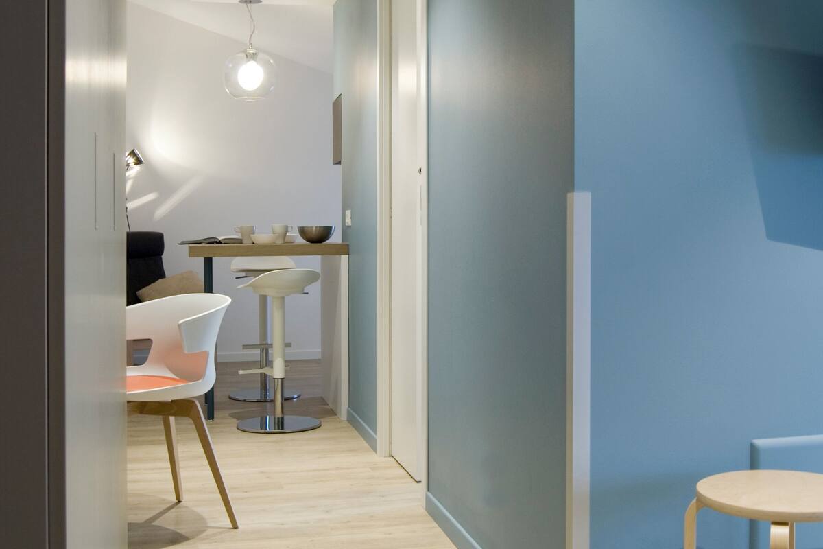 A modern kitchen with a dining area, featuring a white chair, a round table, and a light-colored floor.