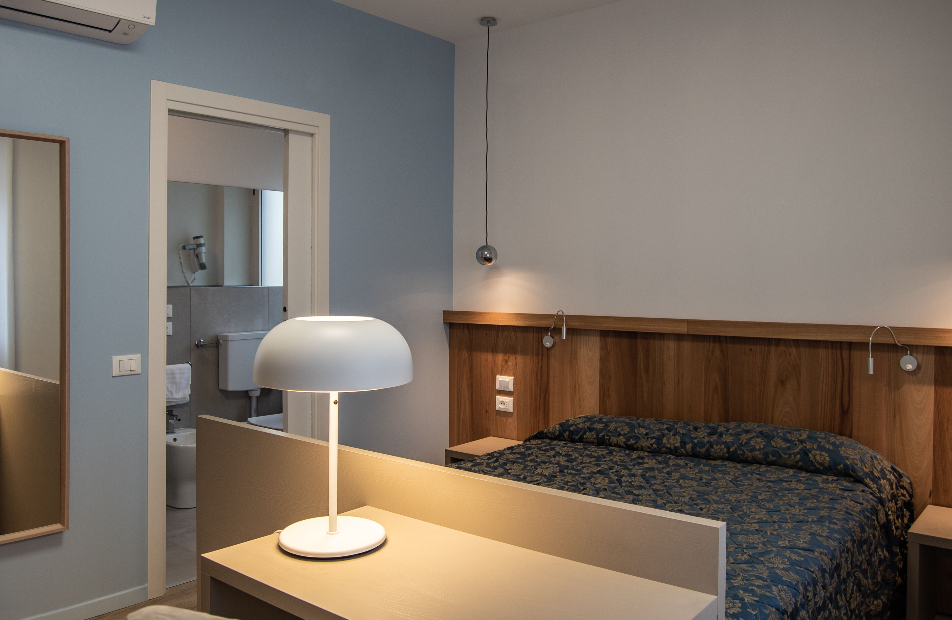 A bedroom with a bed, bedside table, lamp, and a wooden headboard.