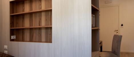 A bedroom with a bed, a wooden bookshelf, a grey chair, and a door.