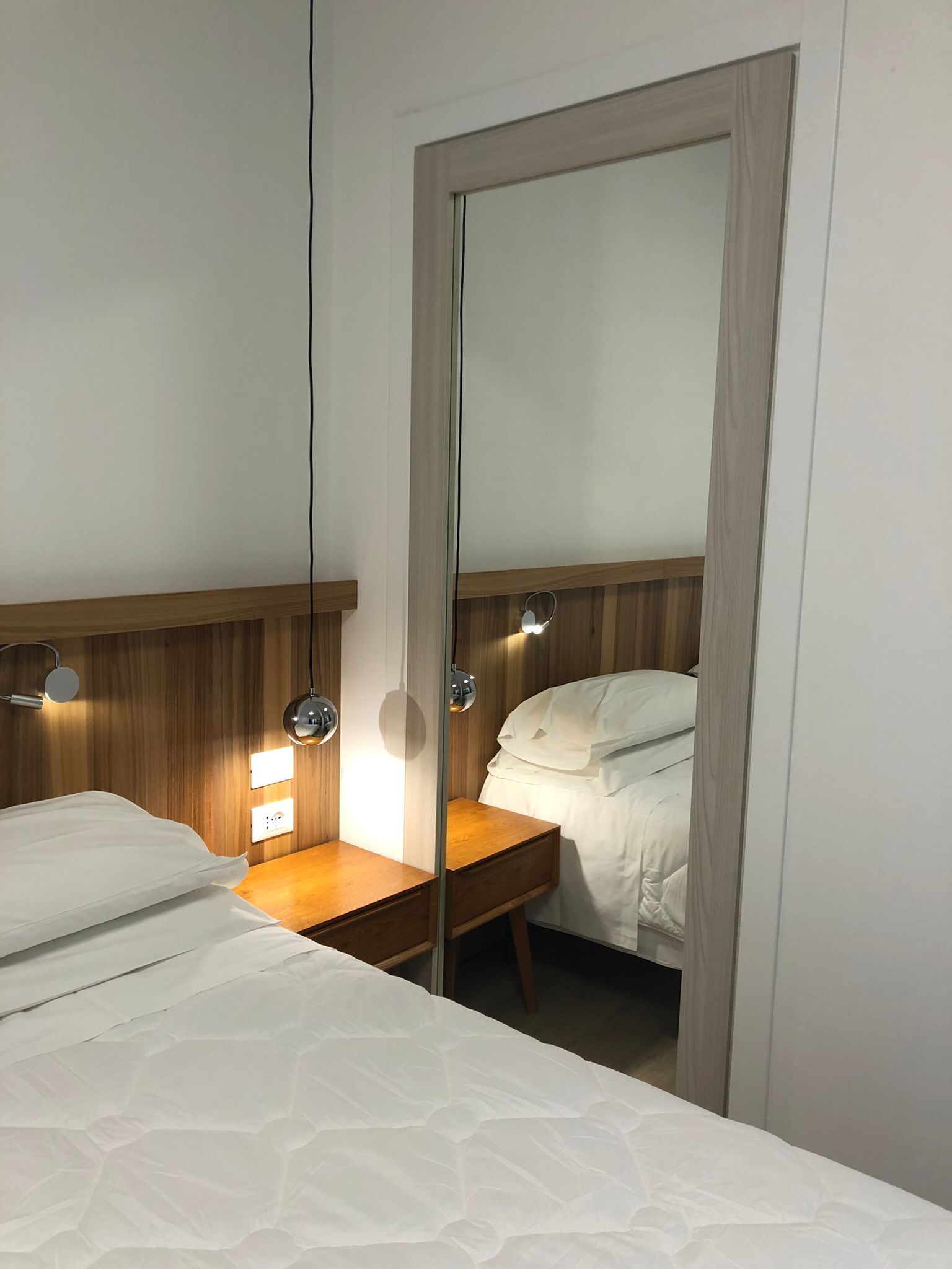 A hotel room with a bed, bedside table, and a mirror.