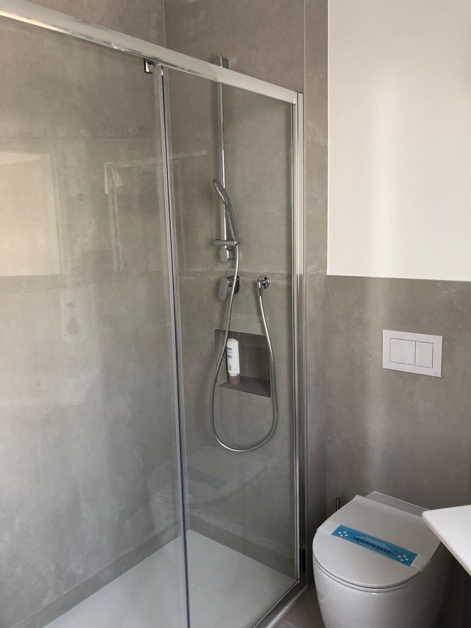 Ein modernes Badezimmer mit einer gläsernen Duschkabine, einer Toilette und einem an der Wand montierten Lichtschalter.