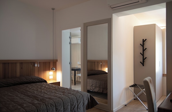 Une chambre avec un grand lit, un bureau et une chaise. Il y a un miroir au mur et un porte-manteau.