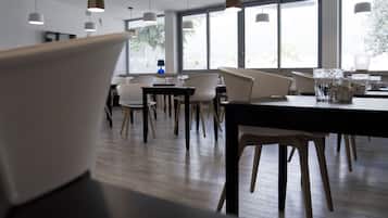 Un comedor moderno con mesas y sillas de madera, iluminación colgante y grandes ventanales que dejan entrar luz natural.