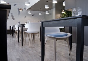 Un espace de salle à manger moderne, avec des chaises blanches et des tables sombres, agrémenté de luminaires suspendus et d’un mur décoratif.