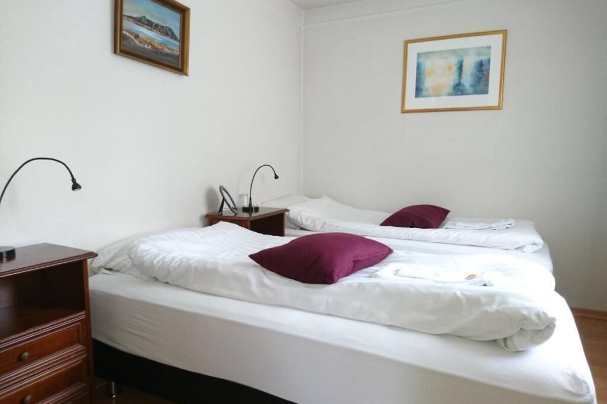 A hotel room with two beds, a wooden dresser, a nightstand with a lamp, and two framed pictures on the walls.