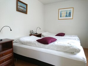 A hotel room with two beds, a wooden dresser, a nightstand with a lamp, and two framed pictures on the walls. - Alba Guesthouse (Reykjavik)