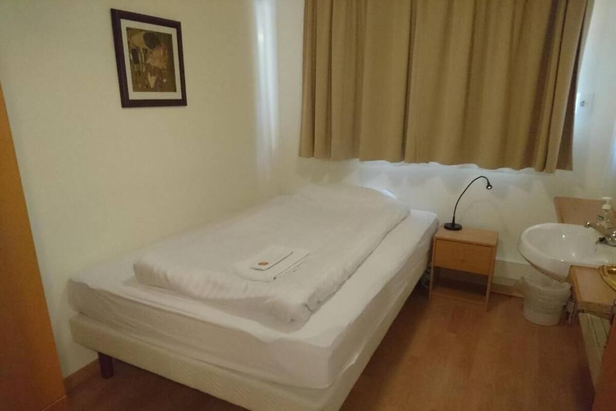 A single bed with a white mattress and a small bedside table with a lamp.