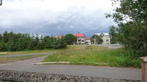 A residential area with a paved road, green trees, and buildings with red roofs. - Alba Guesthouse (Reykjavik)
