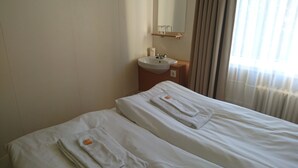 A hotel room with two beds, each with a neatly folded towel and a small orange tag. A sink and mirror are mounted on the wall above the beds.