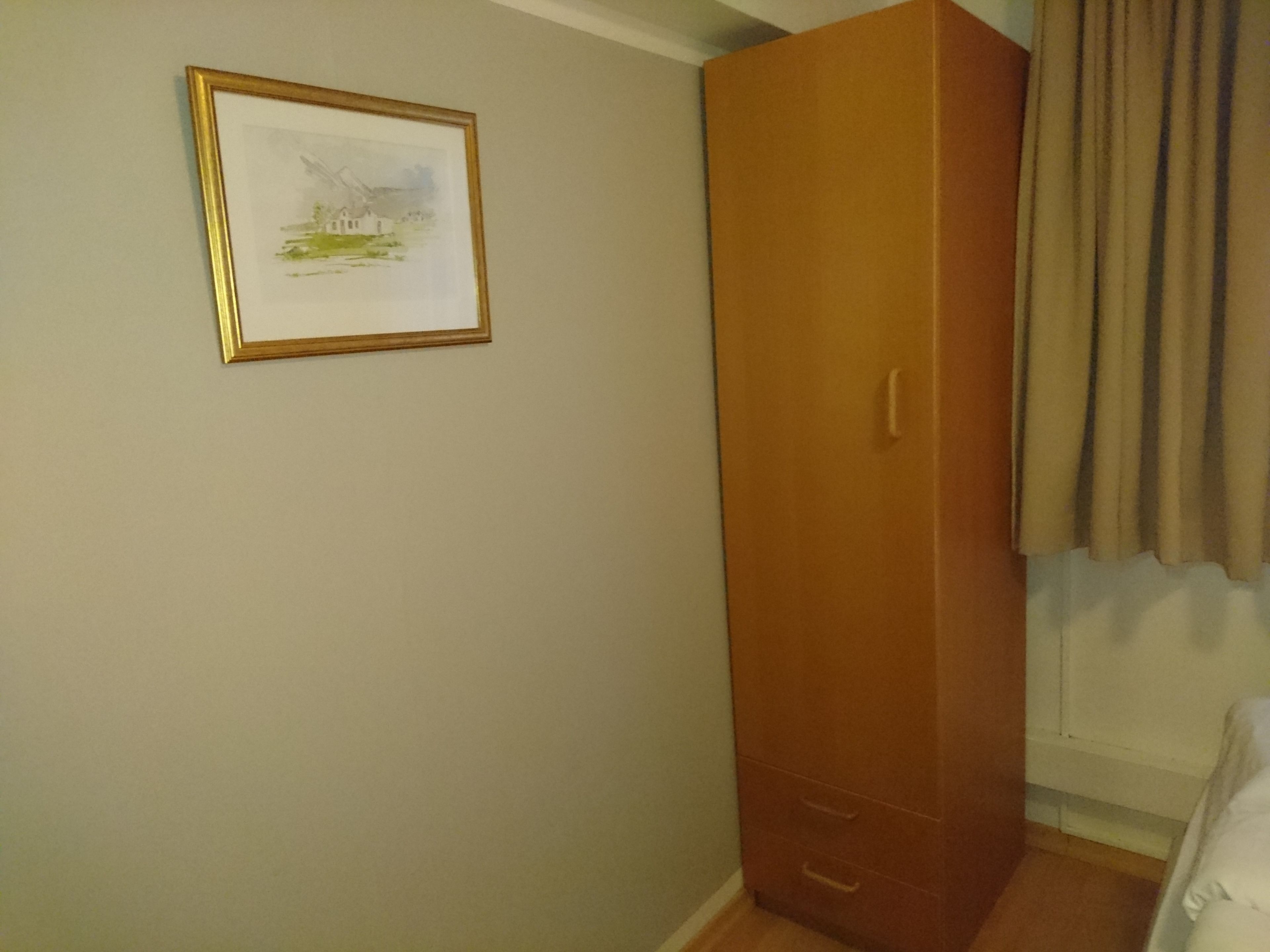 Quarto com guarda-roupa de madeira, quadro na parede e janela com cortinas.