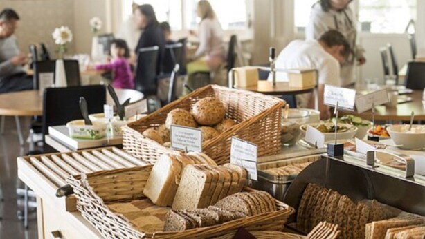 Una sección de panadería con diferentes panes y pasteles exhibidos en cestas, y un cartel que indica el tipo de pan.