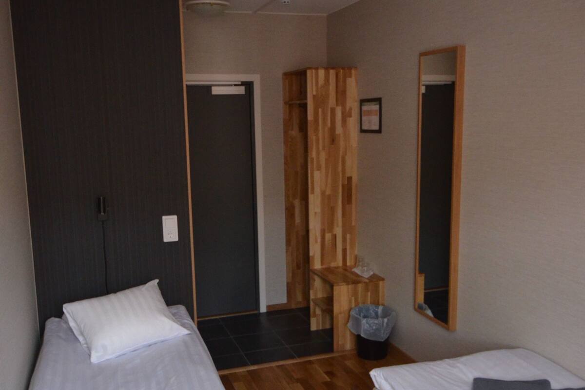 Habitación de hotel con dos camas, piso de madera, un espejo y una puerta que da a otra habitación.