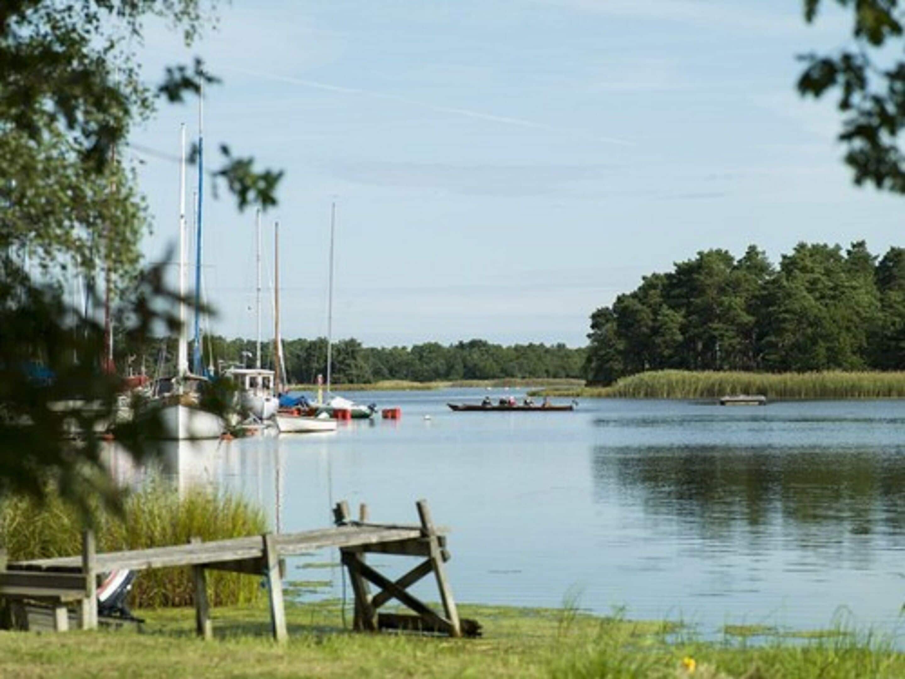 A calm lake with boats, a dock, and a forested area in the background.