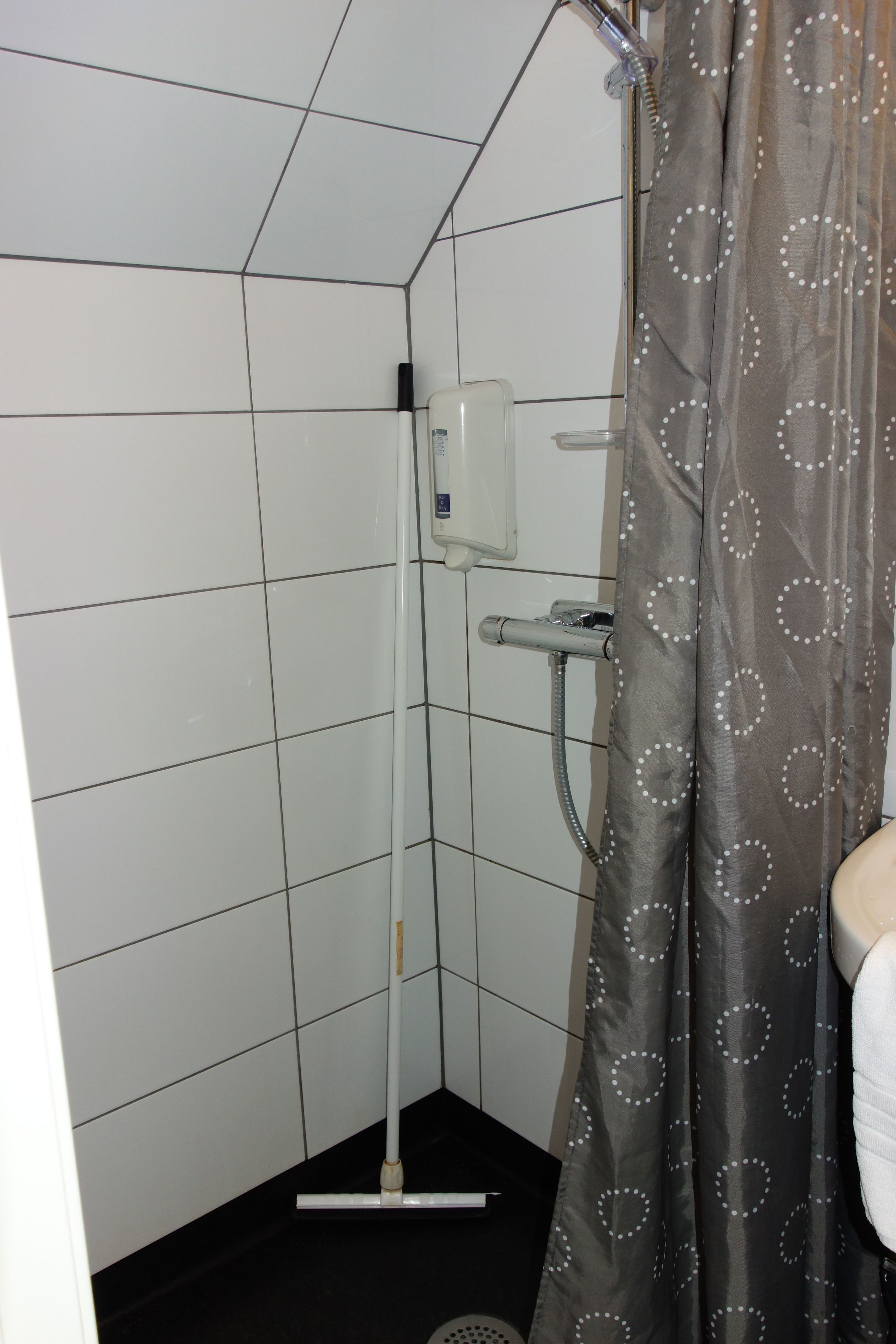 A shower with a grey curtain, white tiled walls, and a handheld showerhead.