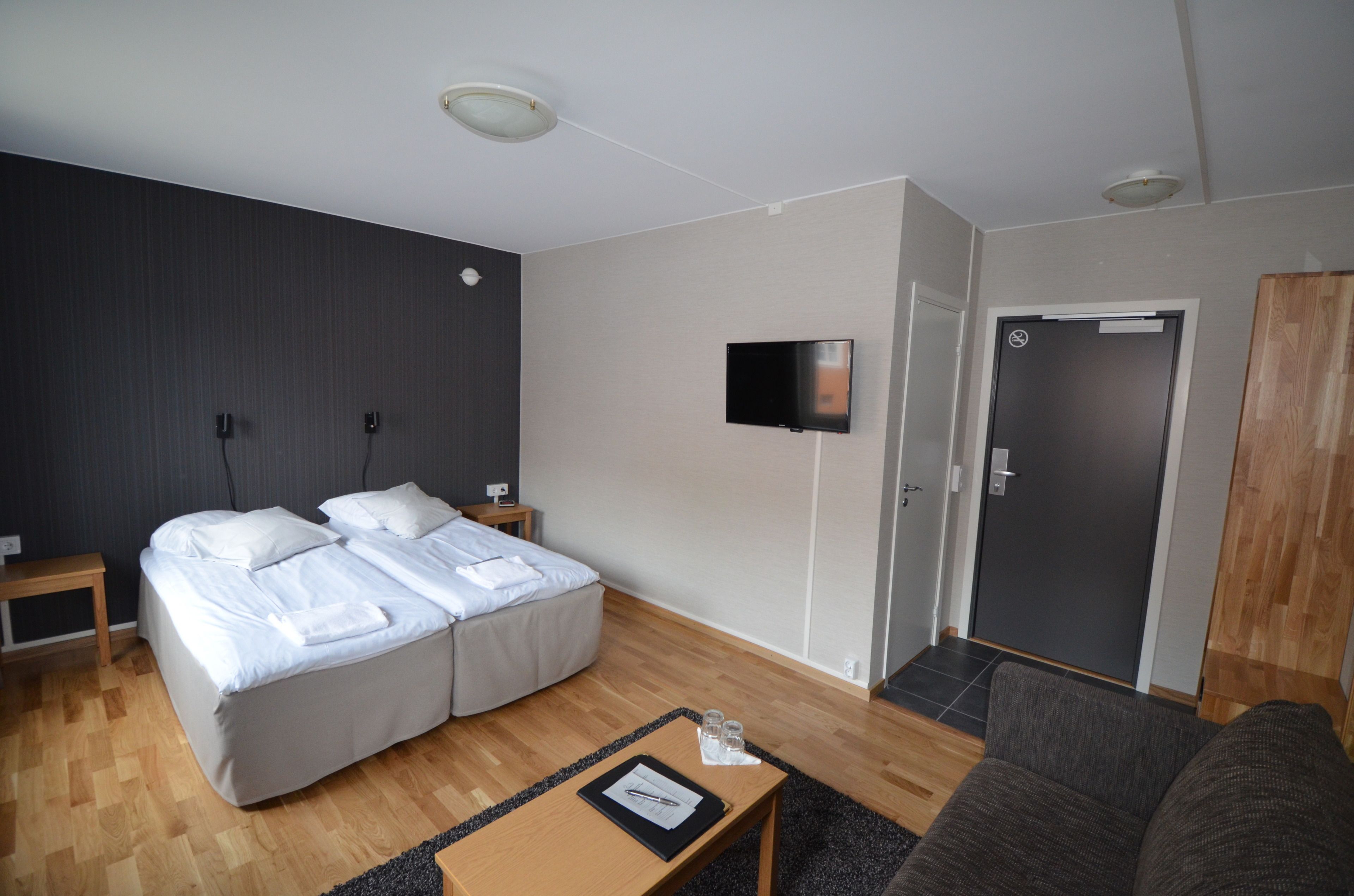 Una habitación de hotel con cama doble, mesitas de noche, un televisor de pantalla plana, armario y sofá.