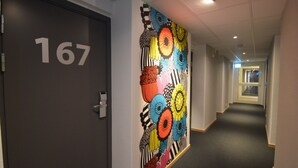 Un pasillo con una puerta marcada con el número 167, un mural floral de colores en la pared y un suelo alfombrado.