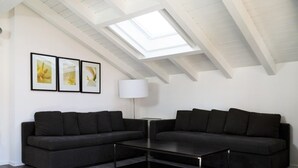 Een moderne woonkamer met dakraam, twee donkere banken, een salontafel en drie ingelijste foto's aan de muur.