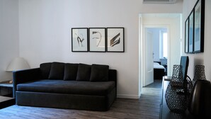 Een moderne woonkamer met een donkere bank, een lamp en lijstwerken aan de muur.