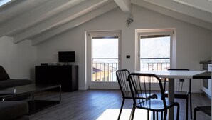 Een modern loft appartement met een schuine plafond, een eethoek met tafel en stoelen, een bank en een tv op een kast.