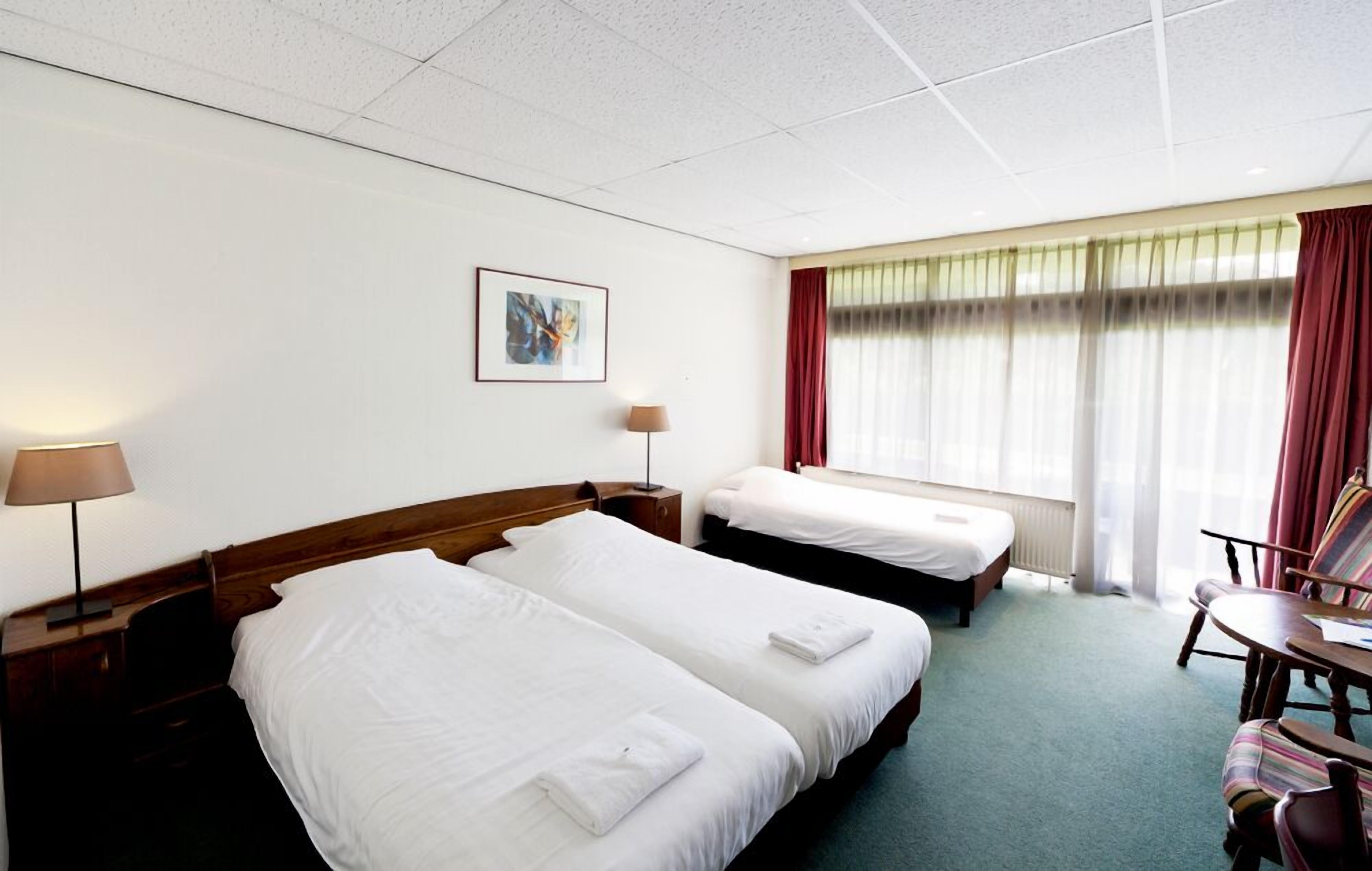 Une chambre d’hôtel avec deux lits, une chaise, un bureau et une fenêtre avec des rideaux.