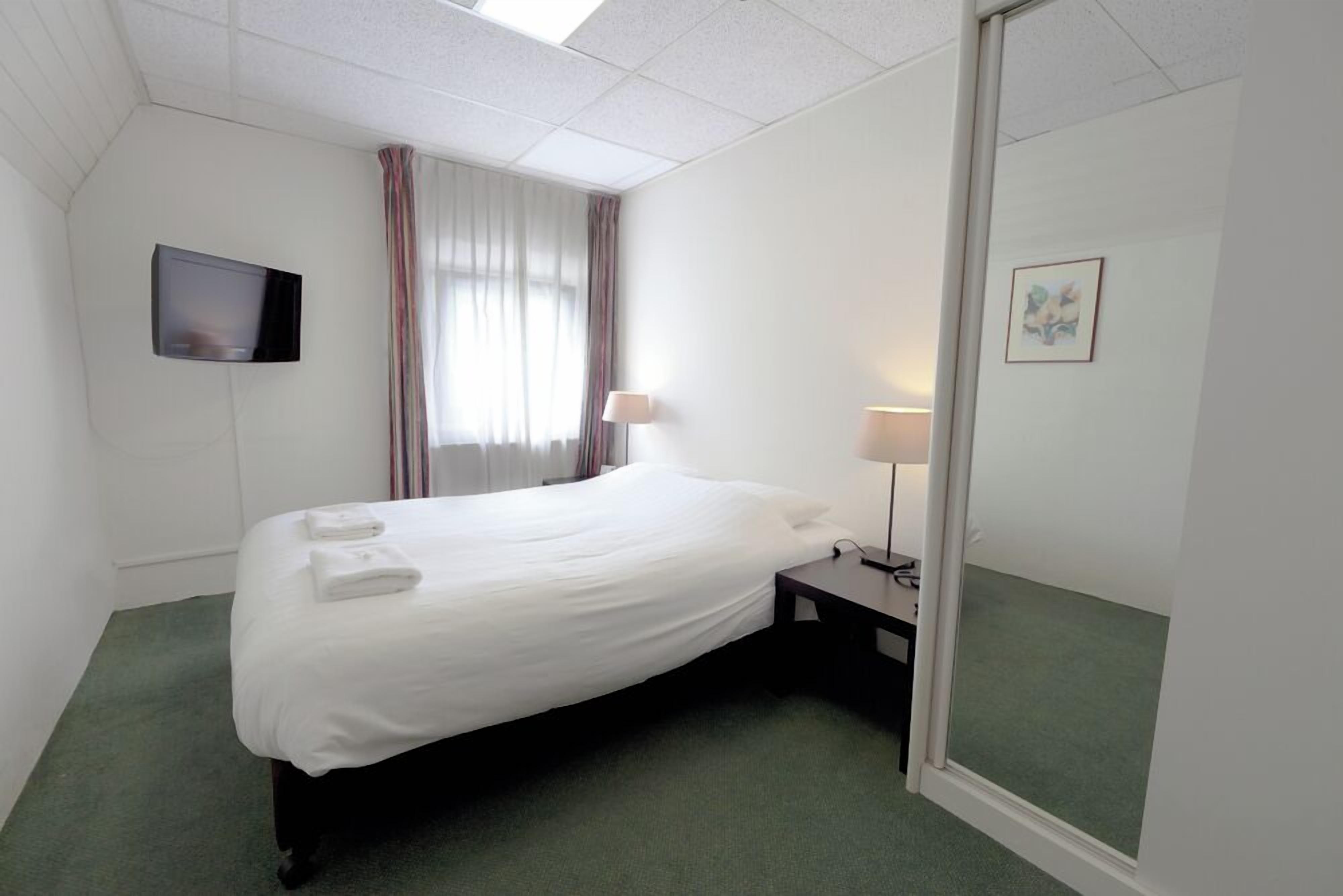 Une chambre d’hôtel avec un lit, une télévision, une lampe et un miroir.