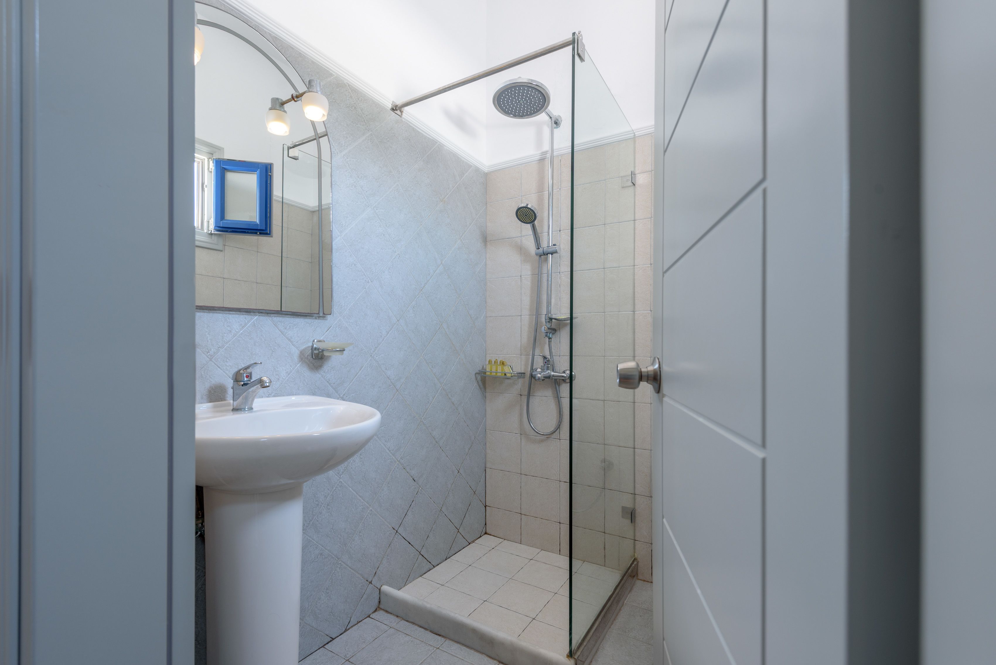 A bathroom with a pedestal sink, a shower with a handheld showerhead, and a glass shower enclosure.