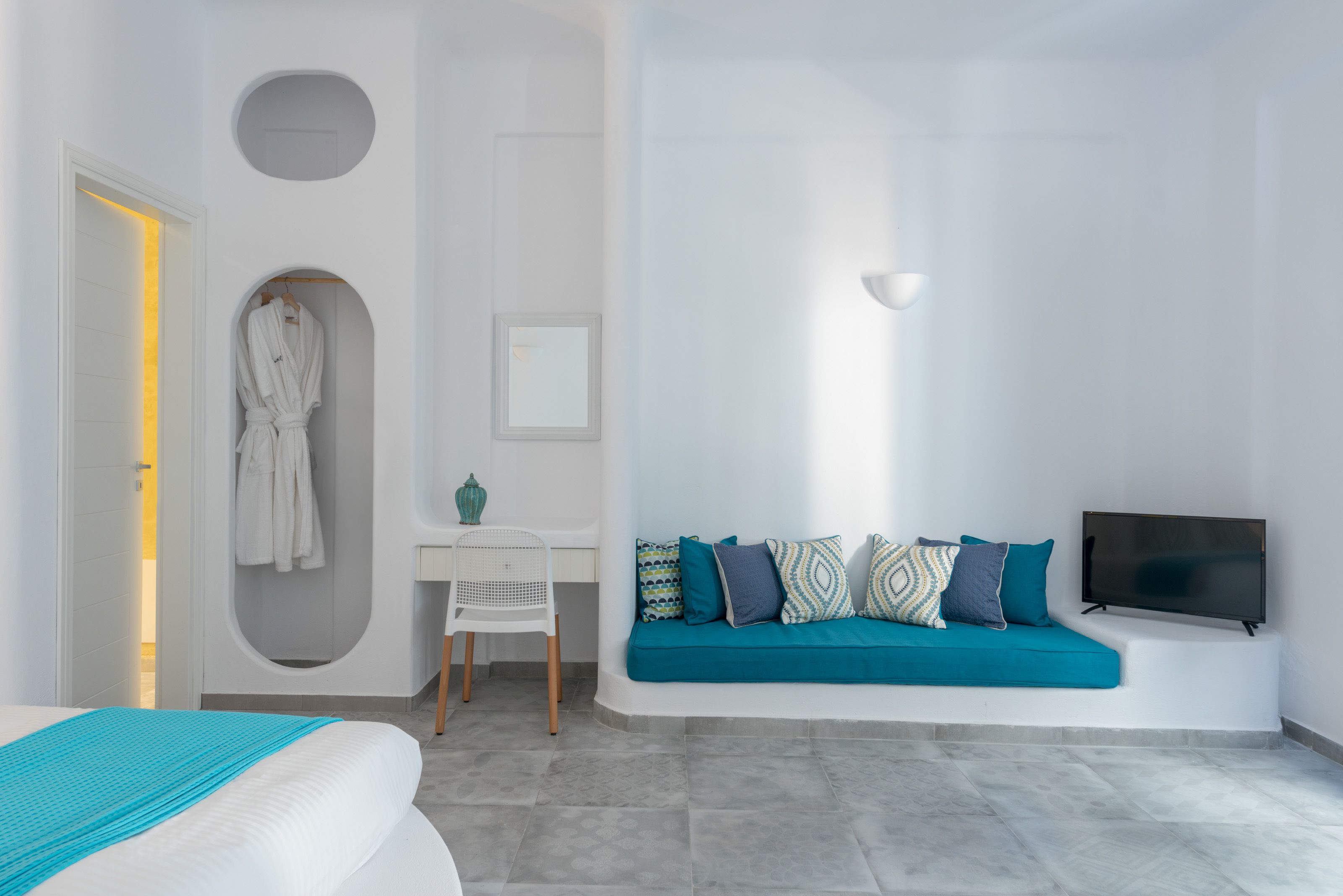 Une chambre moderne avec un lit, un canapé bleu, une télévision et une salle de bain équipée d’une baignoire et d’un peignoir suspendu.