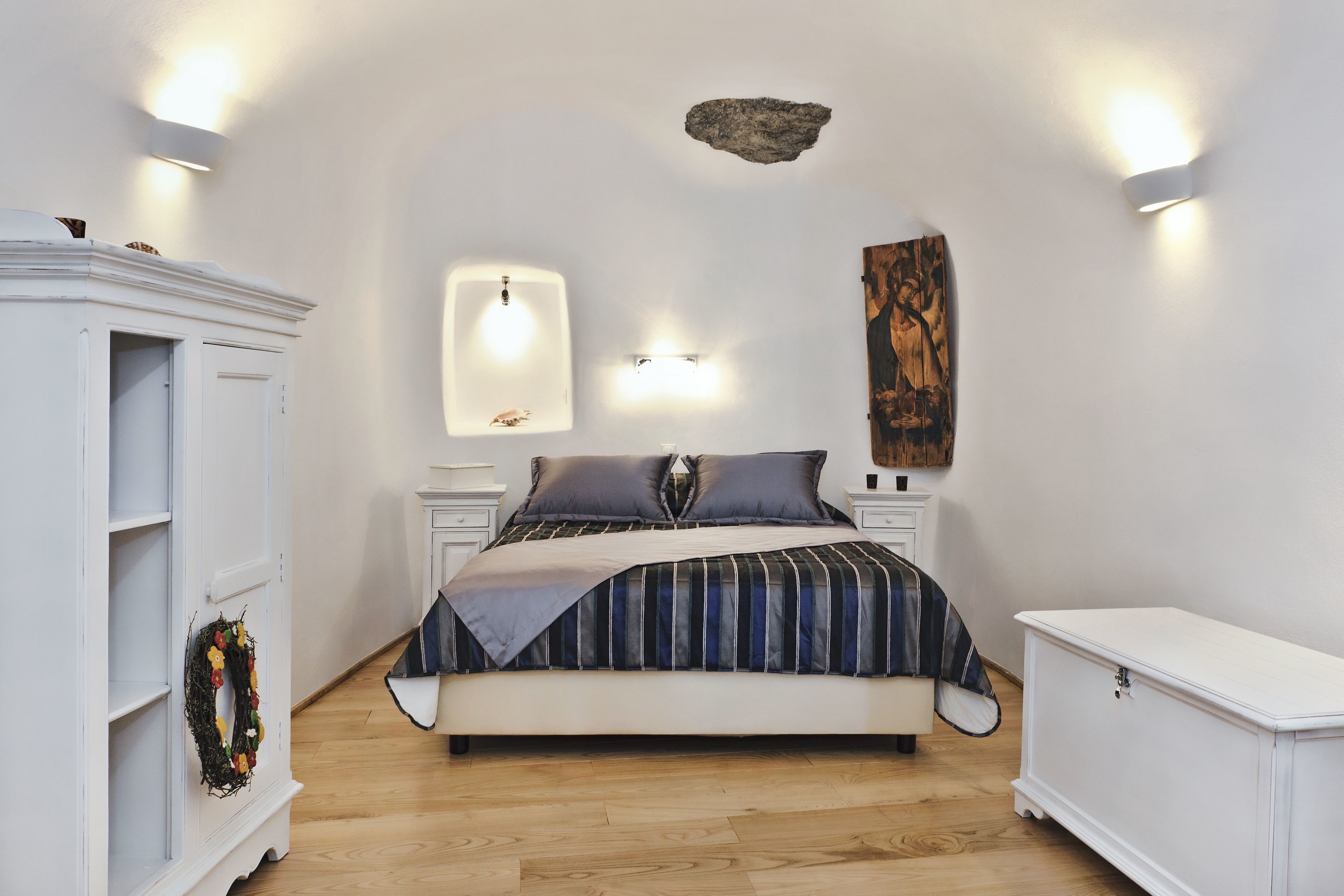 A bedroom with a bed, nightstands, a dresser, and wall-mounted lighting.
