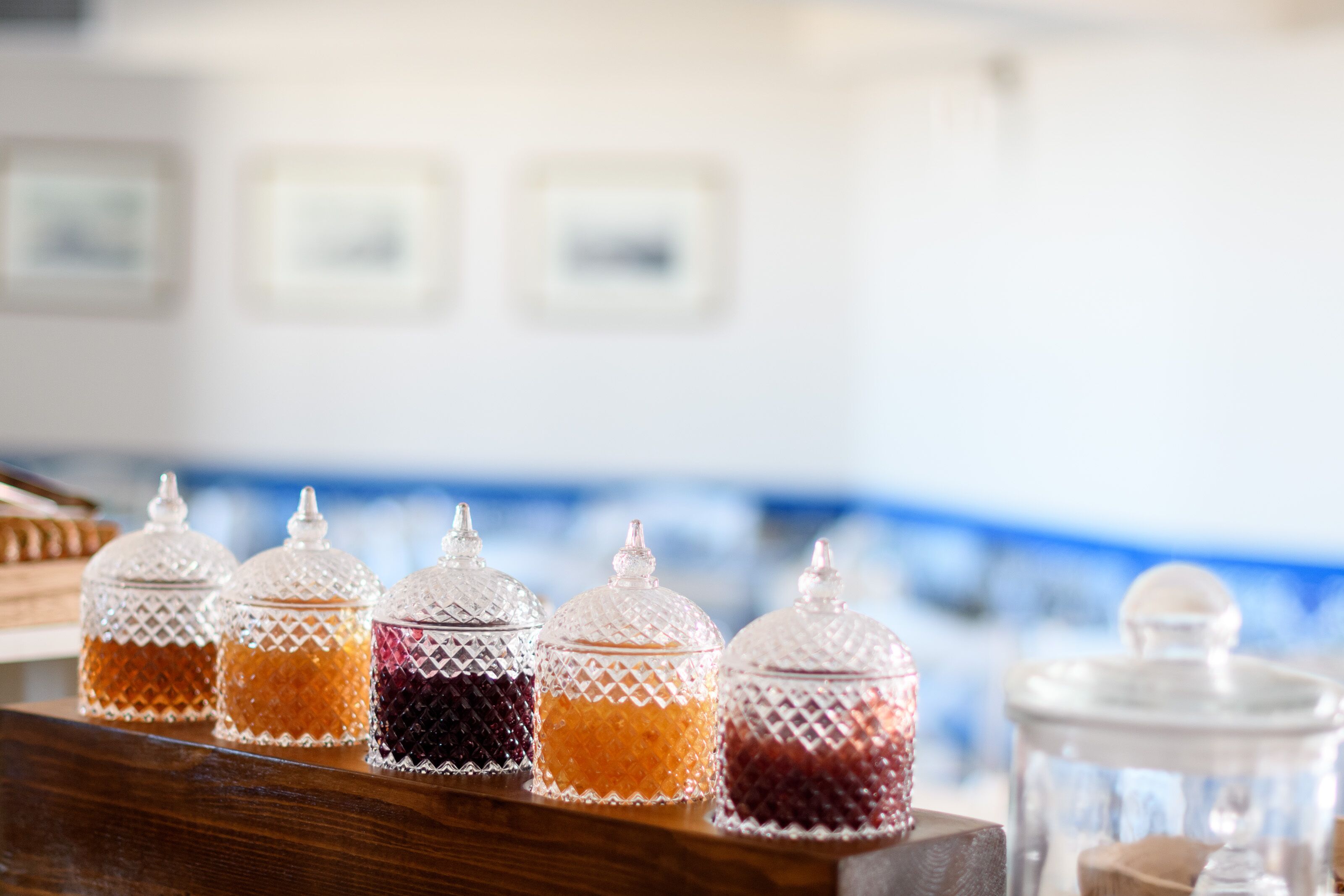 A row of clear glass condiment jars with textured lids on a wooden surface.