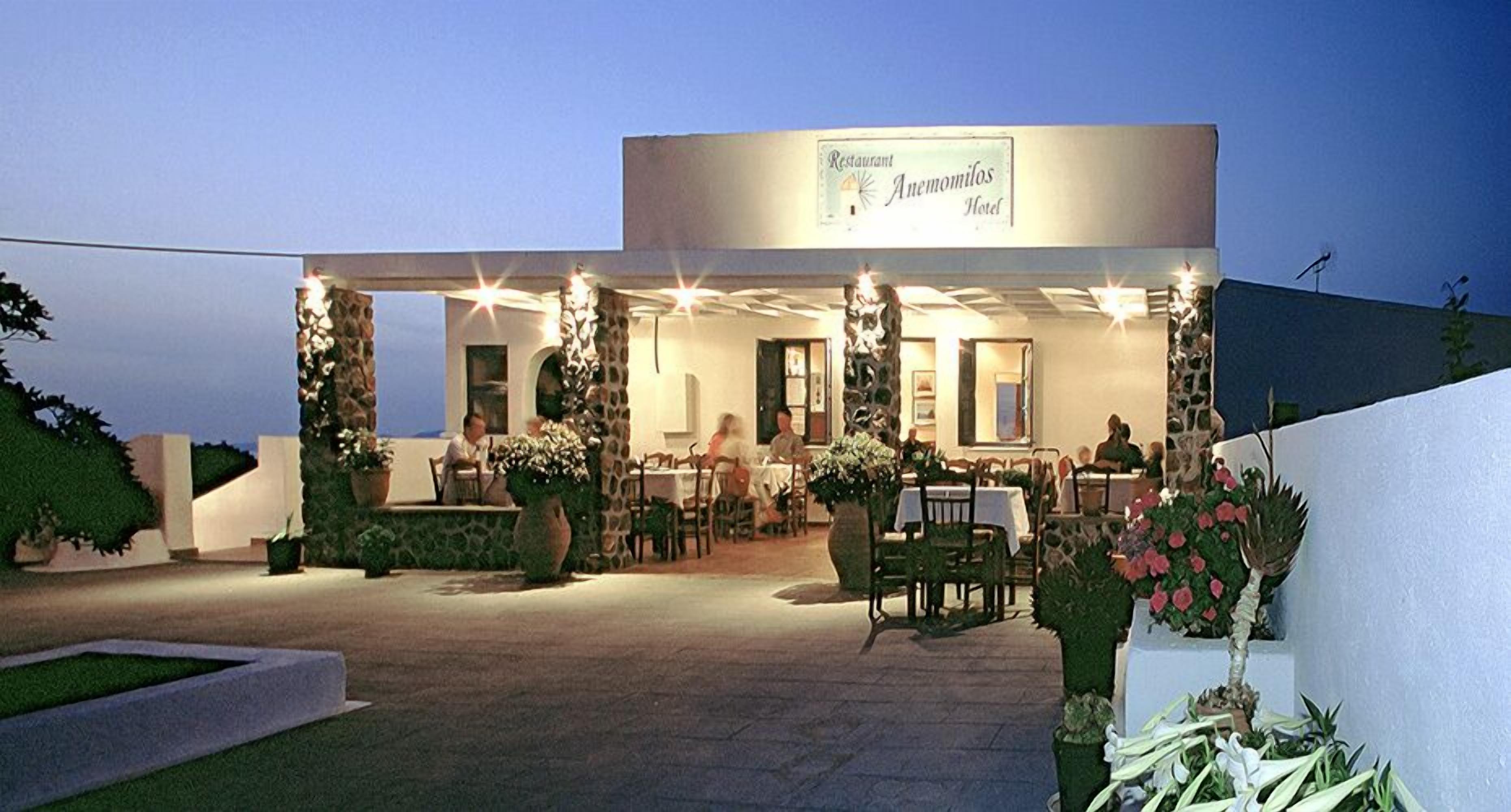 Un restaurante con terraza, un letrero que dice "Anemomilas Hotel" y plantas en macetas alrededor de las mesas.